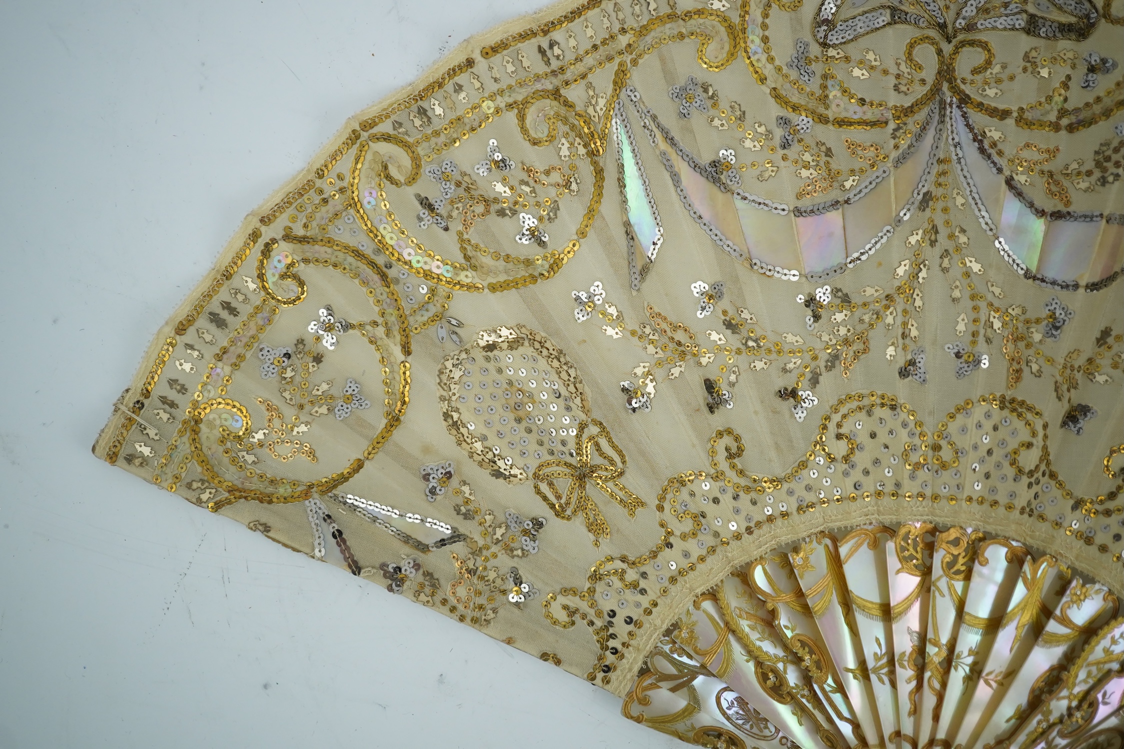 Three French fans: a mother of pearl and sequin fan boxed, a painted silk, feather and bone fan and a gilt decorated bone figural paper fan, the two bone fans having gilt mirrored mounts on the guards, figural paper fan